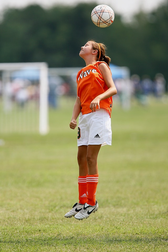 girl jumping in the air to headbutt a soccer ball