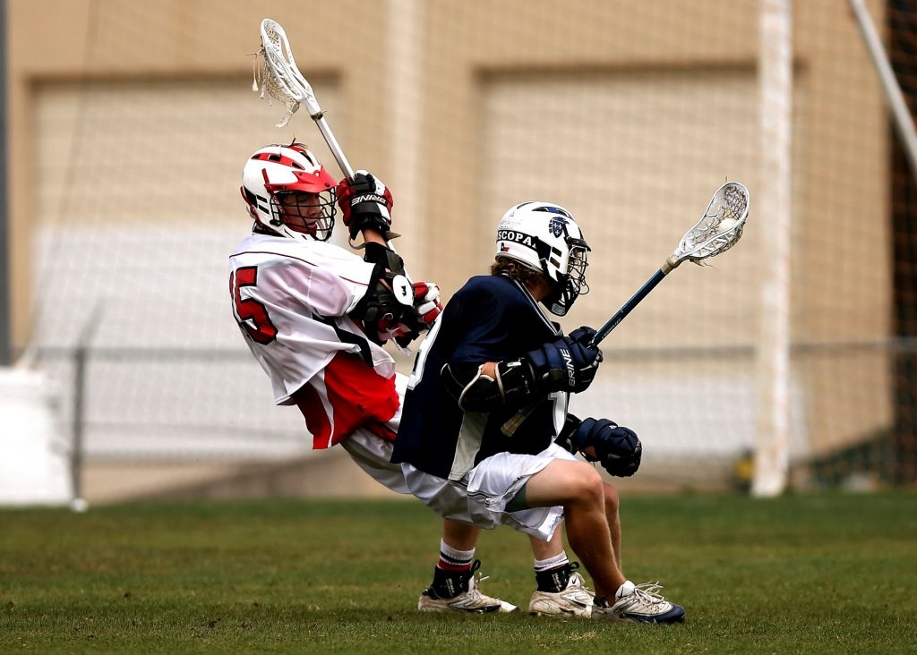 2 men playing lacrosse with helmets action of pivoting