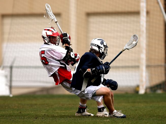 2 men playing lacrosse with helmets action of pivoting