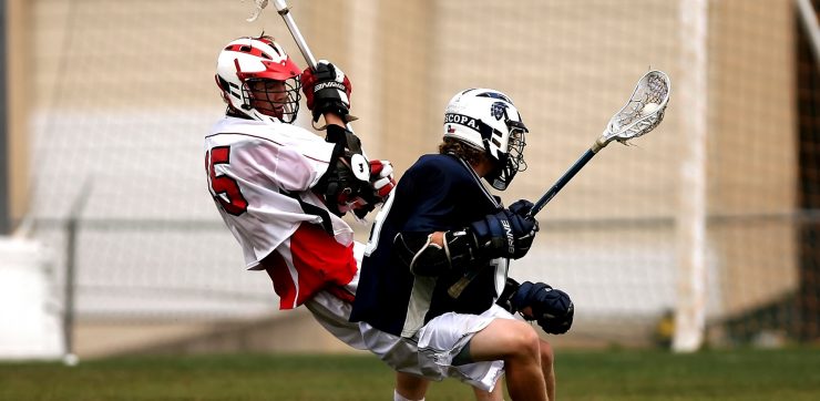 2 men playing lacrosse with helmets action of pivoting