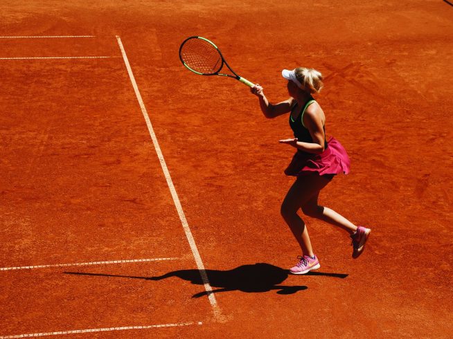 woman playing tennis on a dirt court with ball in air