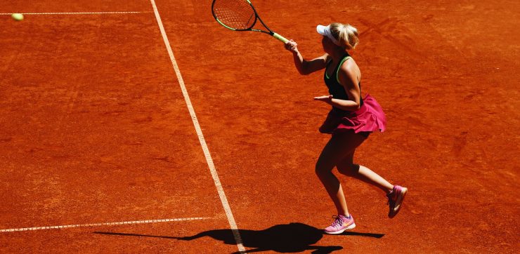 woman playing tennis on a dirt court with ball in air